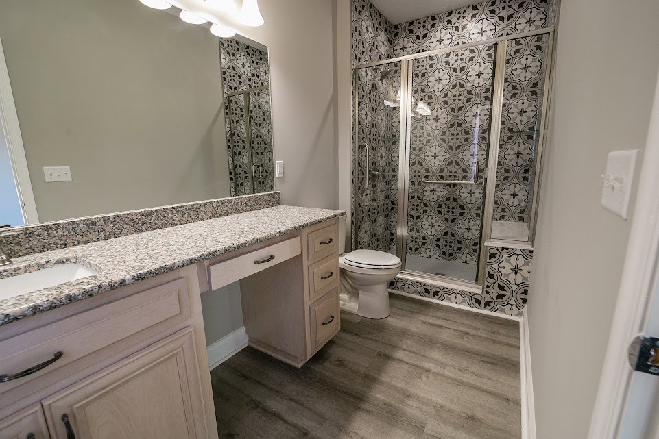 Bathroom featuring a marble countertop vanity, glass-enclosed shower with tile walls, white toilet, chrome faucet, overhead recessed lighting, and light-colored cabinetry with