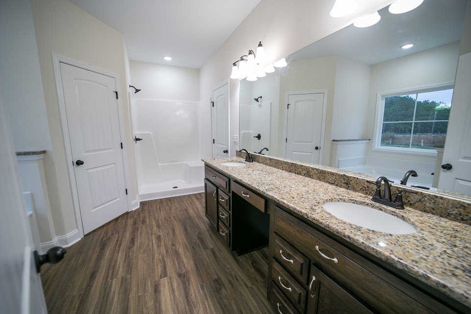 Bathroom featuring a marble countertop with undermount sink, large wall mirror, freestanding tub, white door with black hardware, and window overlooking trees.