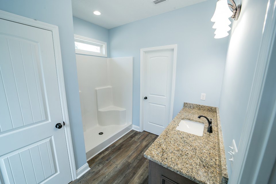 Bathroom with marble countertop, undermount sink, glass-enclosed shower with white tile, white door with black knob, chrome faucet, and neutral wall finishes