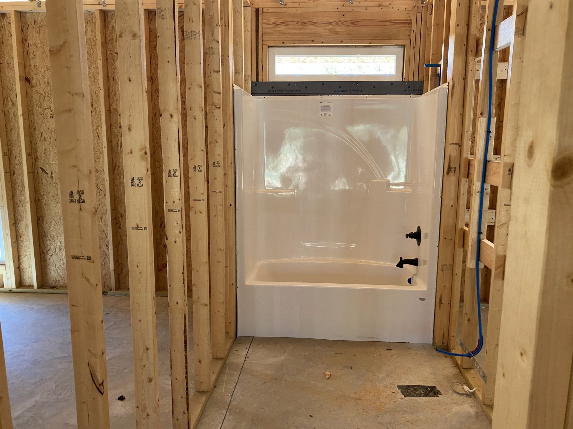 Bathroom with white shower featuring black faucet, wood-paneled wall, blue-painted window frame, and plaster surfaces