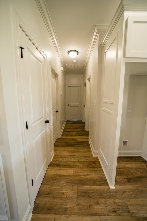 Hallway with white paneled doors featuring black handles, smooth white walls, and warm wood flooring