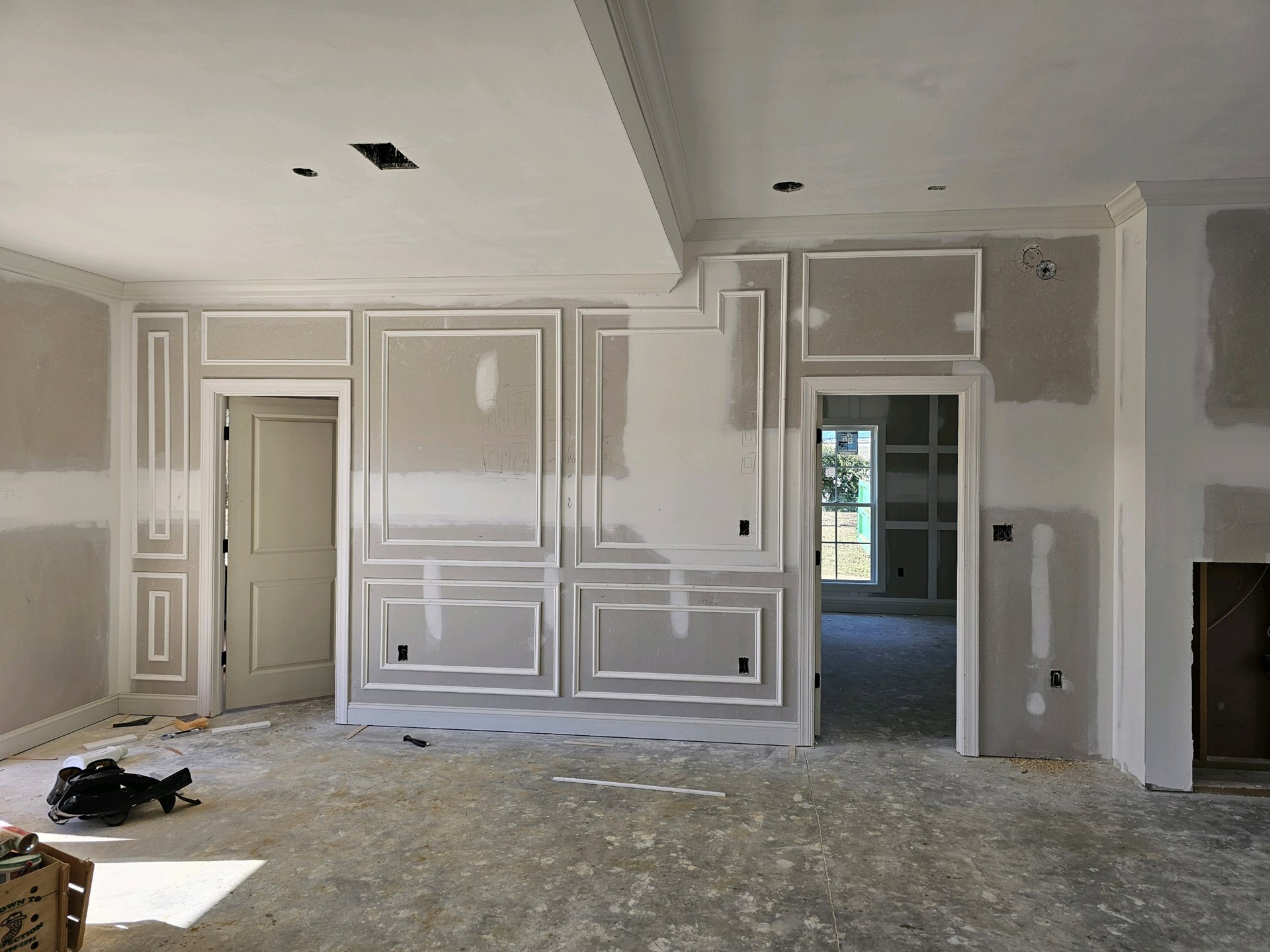 White-walled room with white trim, white door and frame, wooden crate holding a magnifying glass and can, black belt on white surface, window with green door.