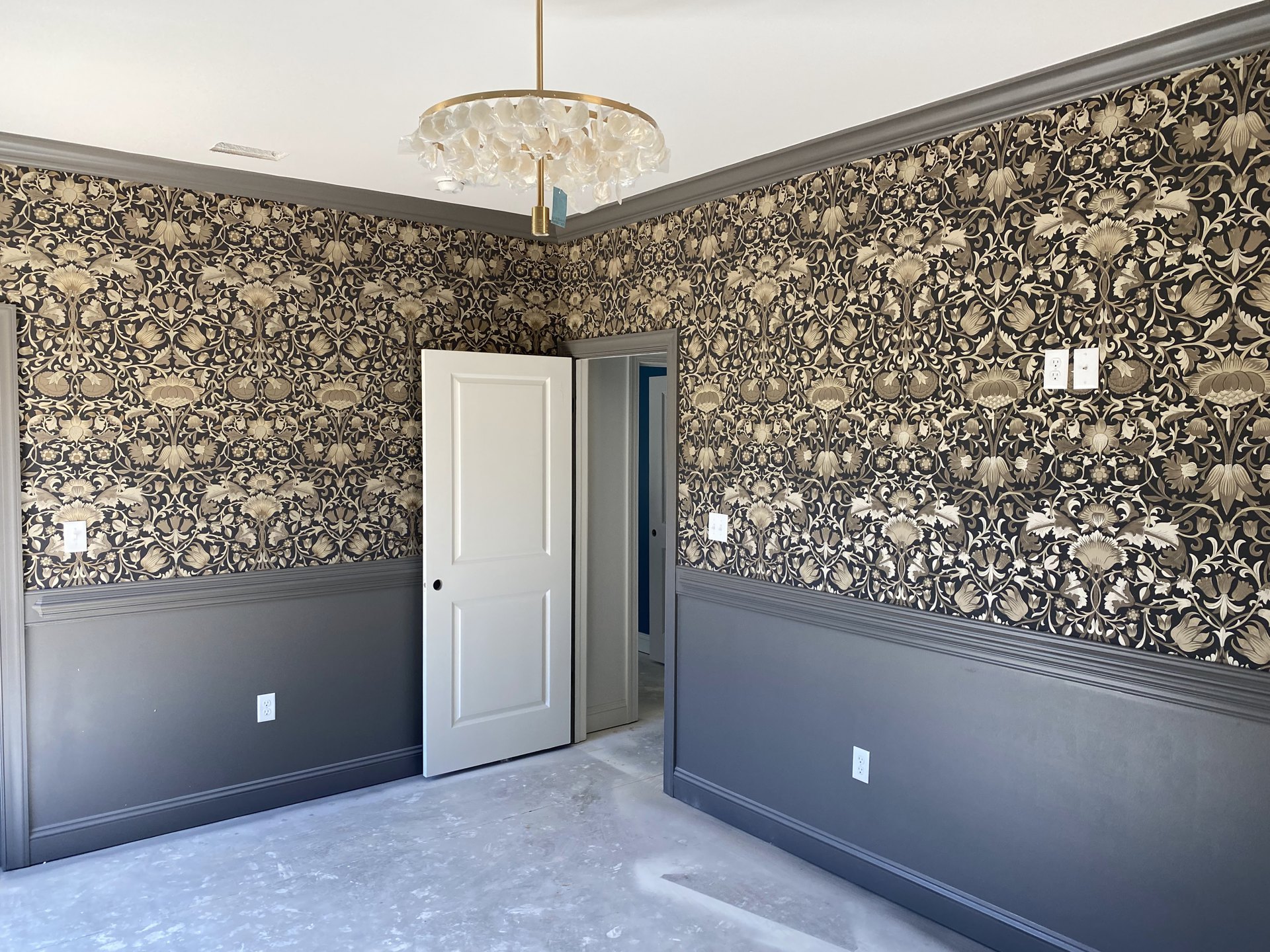 Chandelier with clear plastic cup accents hanging from white plaster ceiling, black and white patterned wallpaper covering walls, white door with circular cutout, blue door