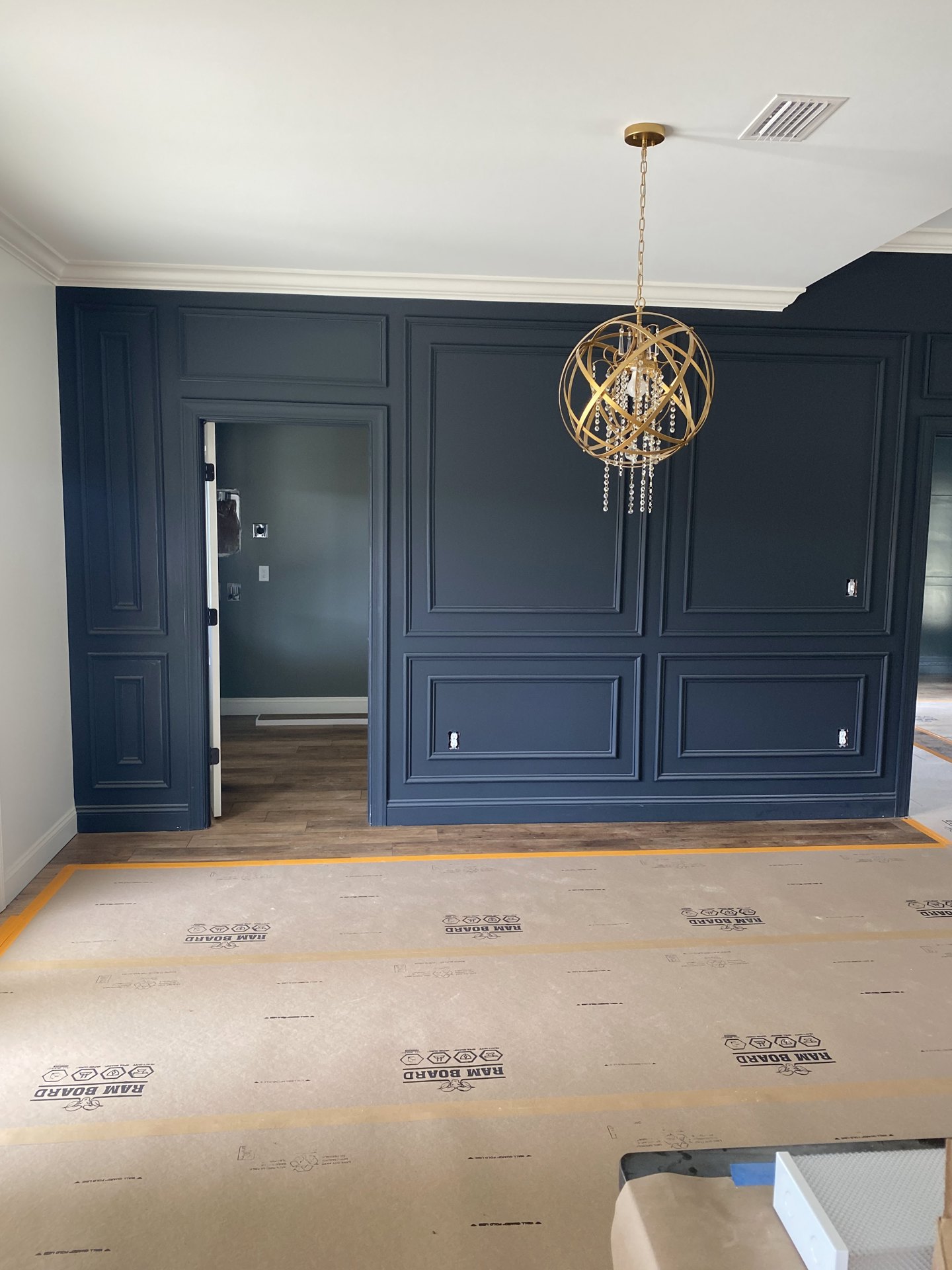 Chandelier with crystal accents hanging from a chain over a carpeted floor, white plaster walls with crown molding, wooden door, and recessed ceiling.