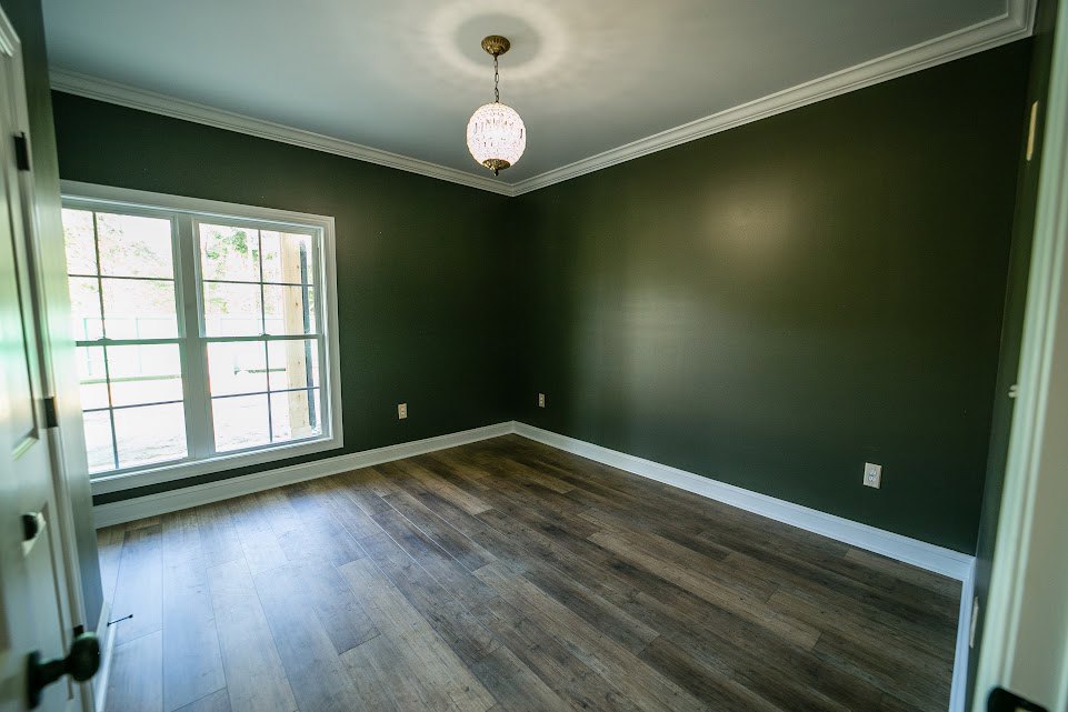 Wood flooring in a bright room with multi-pane window, white plaster walls, and ceiling.