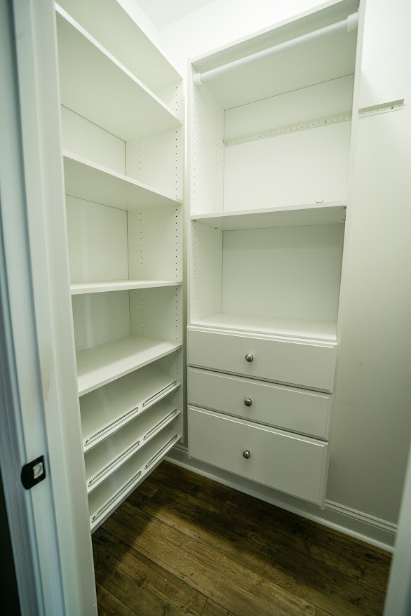 White closet with built-in shelves, drawers, and cabinetry, featuring wood flooring and minimalist interior design.