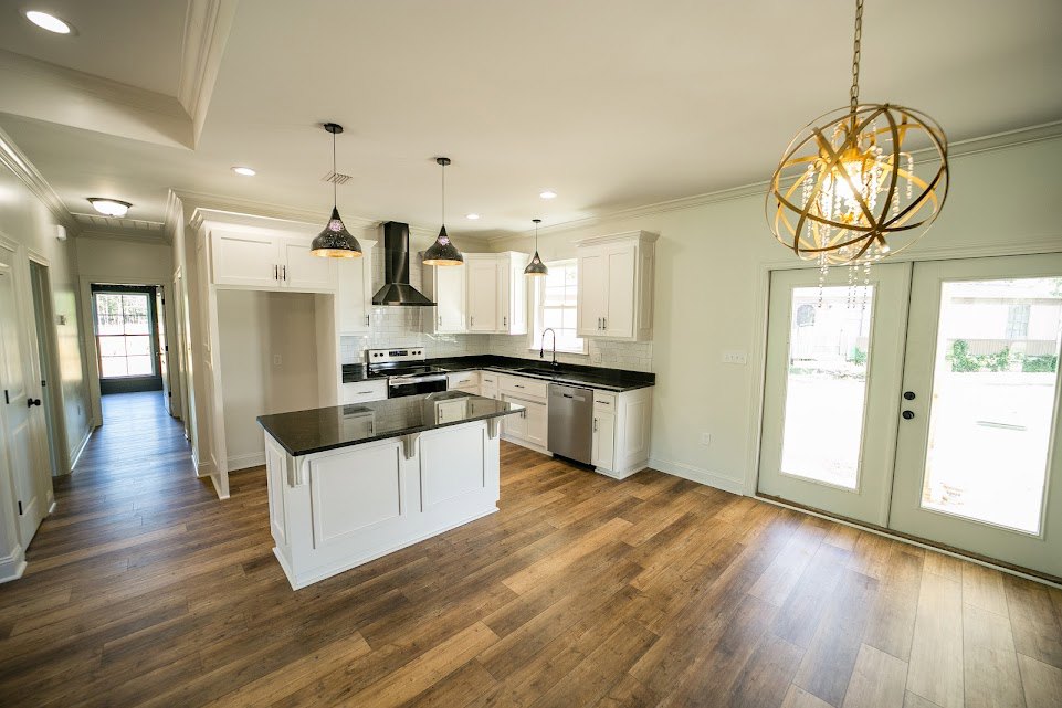 Kitchen with wood flooring, white island featuring black countertops, ceiling light fixture, ceiling vent, white door with window, double glass-paneled doors, white cabinetry