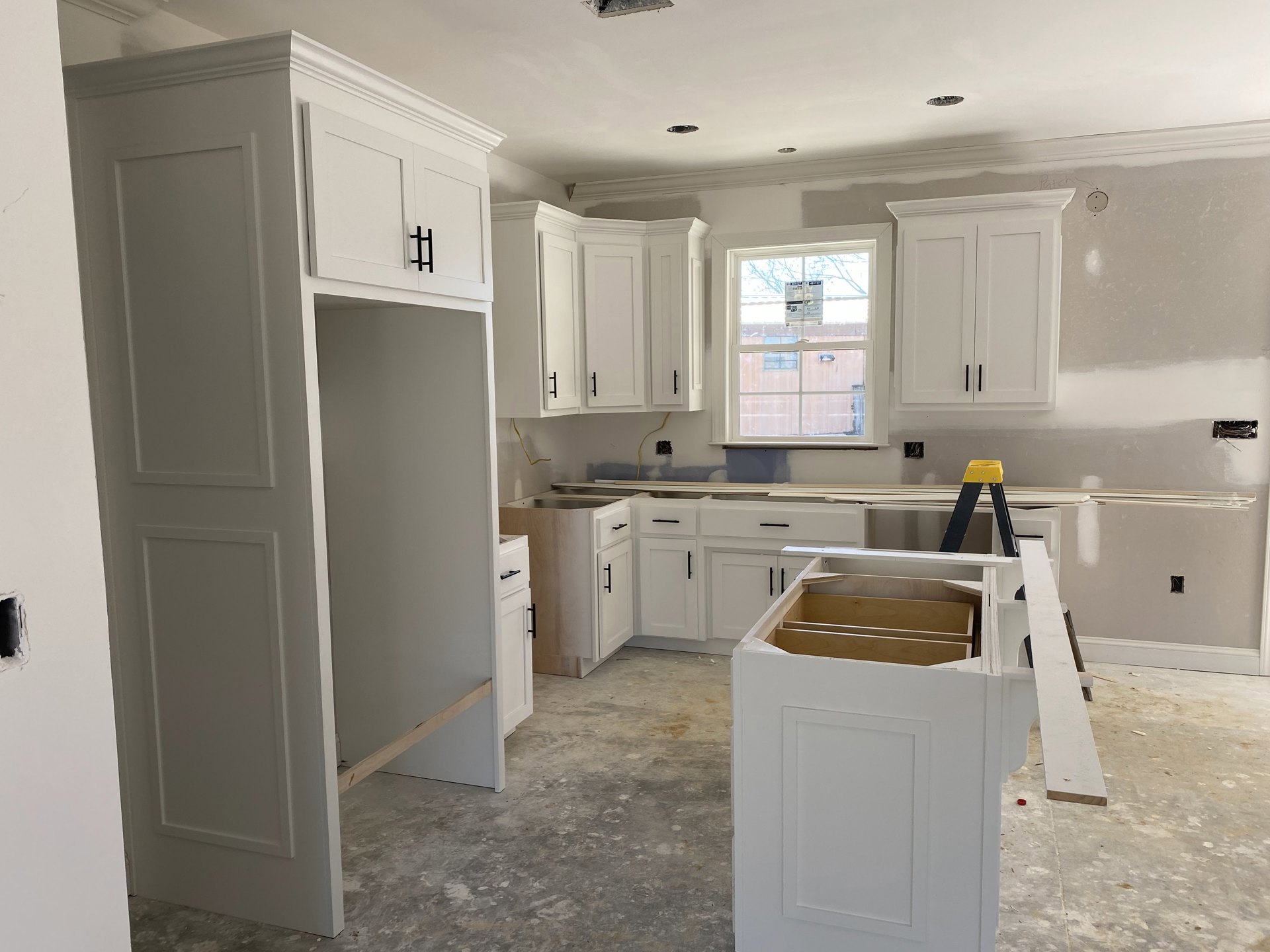 White kitchen with shaker cabinets, black handles, quartz countertops, stainless steel sink, and a window above the workspace.