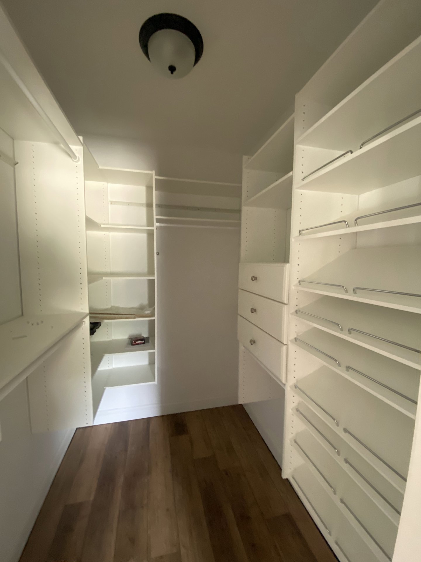 White closet with built-in shelves, wood floor with white base trim, recessed ceiling light, white walls, and metal hanging rods.