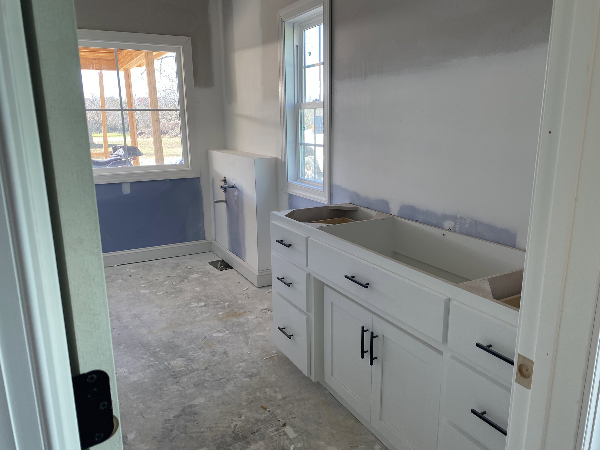 White shaker cabinets, stainless steel sink with chrome faucet, wood-framed window with divided panes, light stone countertop, white tile backsplash