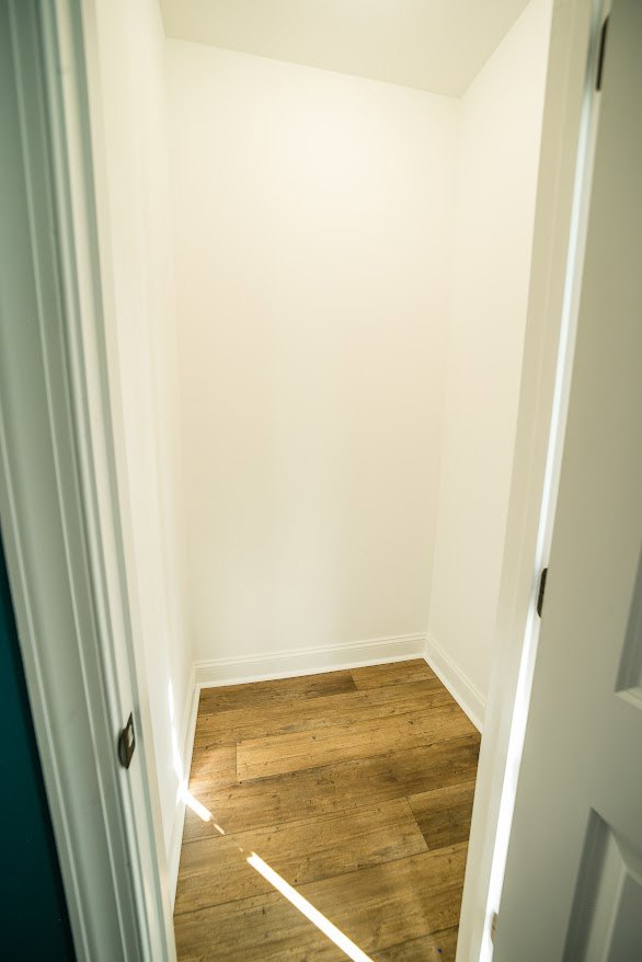 Hallway with light wood flooring, white plaster walls, recessed ceiling lights, and modern door handles