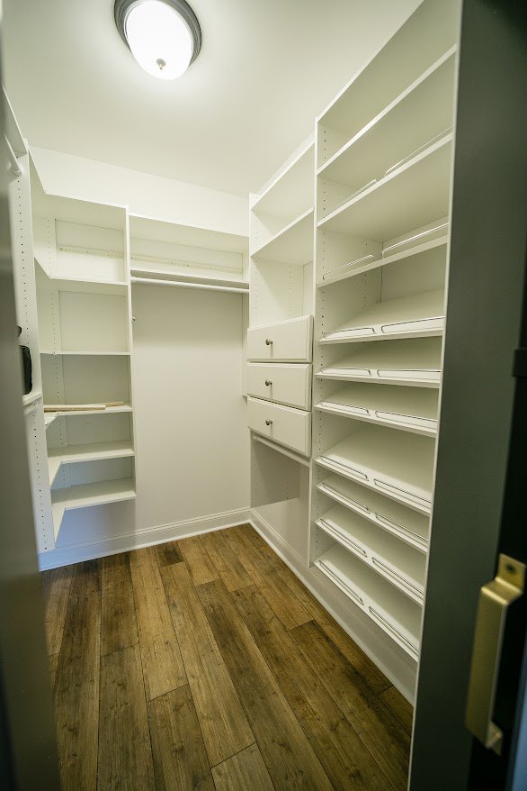 Walk-in closet with white shelving units, hardwood floor, and plaster walls