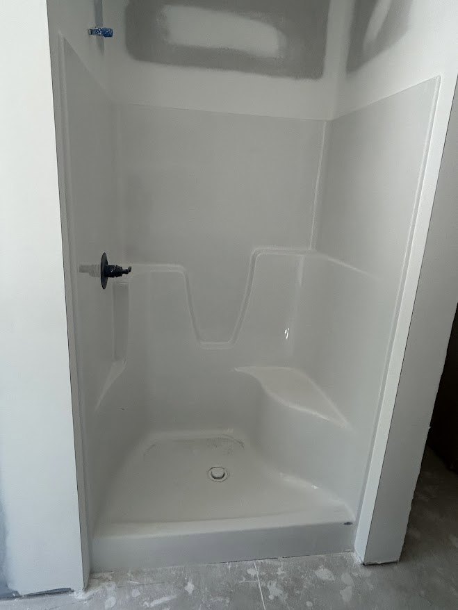 Walk-in shower with exposed plumbing pipe, white marble walls, and plaster surfaces