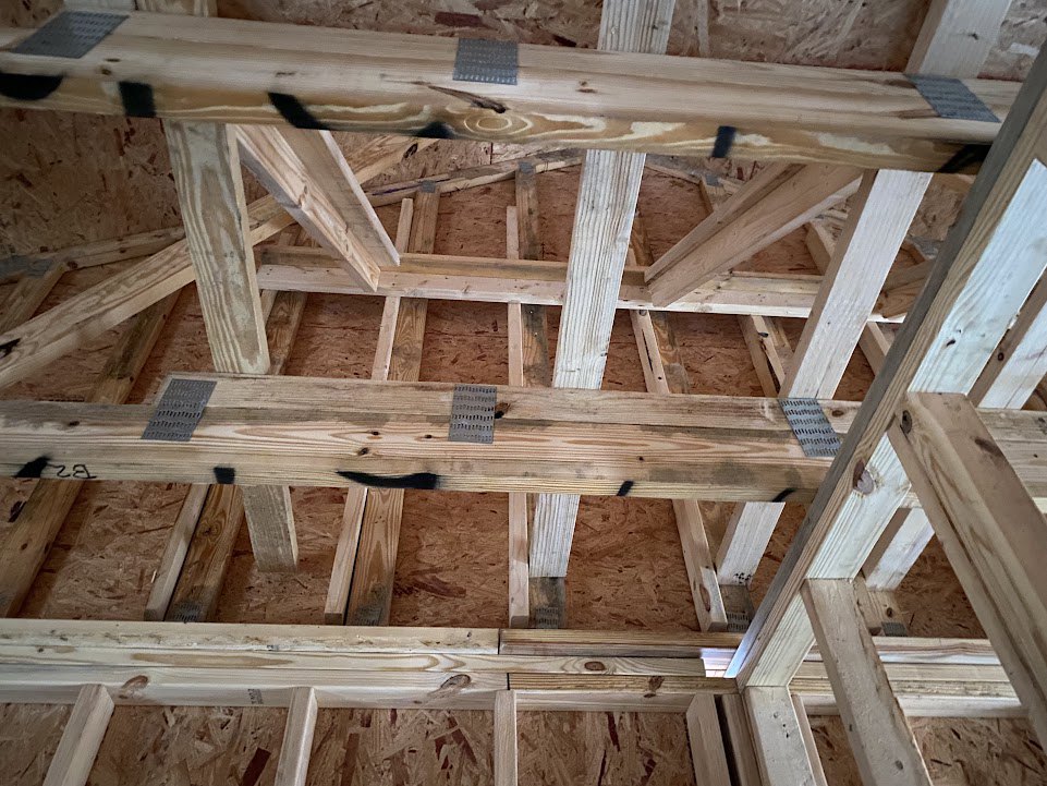 Exposed wood beams and framing in a partially constructed home interior, unfinished lumber and insulation visible
