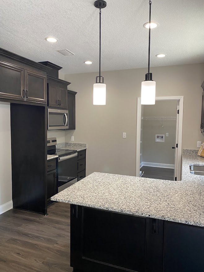 Kitchen with polished granite countertop, black base cabinets, wood flooring, white walls, built-in microwave oven, and a closet featuring a white shelf.