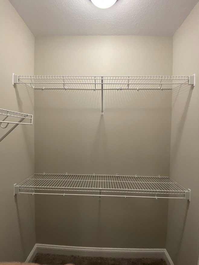 White wire shelving and metal rods in a walk-in closet with grey walls and built-in lighting