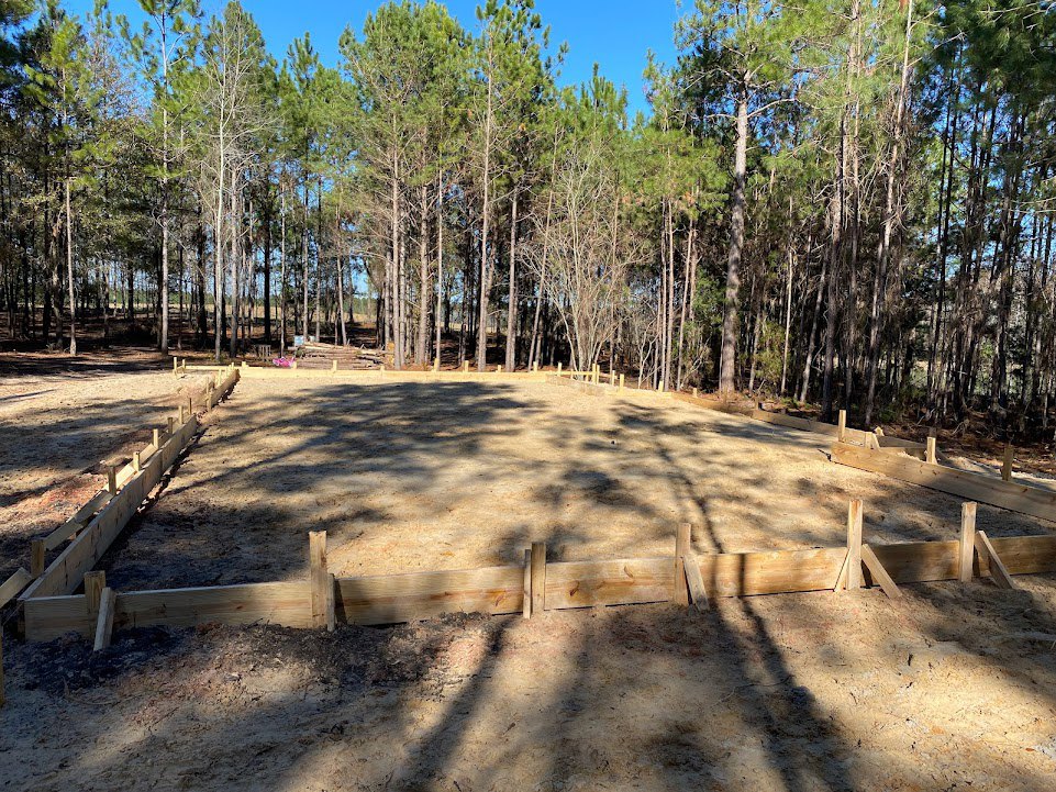Wooden fence bordering a dirt field with scattered trees and blue sky in the background