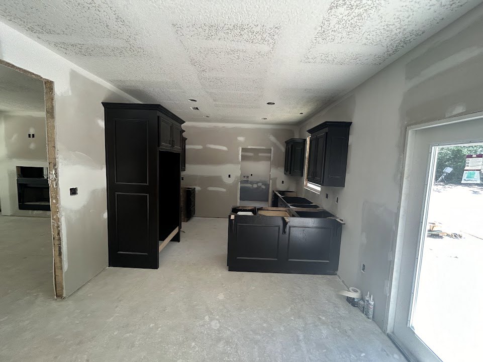 Modern kitchen featuring black cabinetry with open doors, white plaster walls, built-in shelving, and light flooring; a white object sits on a corner shelf.