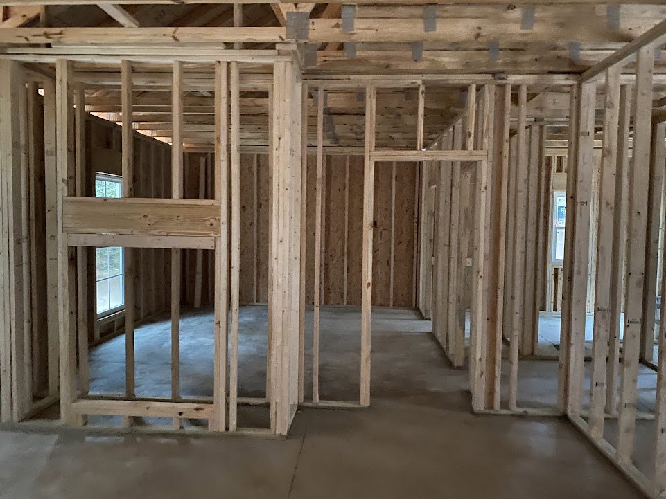 Room under construction featuring exposed wooden beams, unfinished walls, and a large window allowing natural light