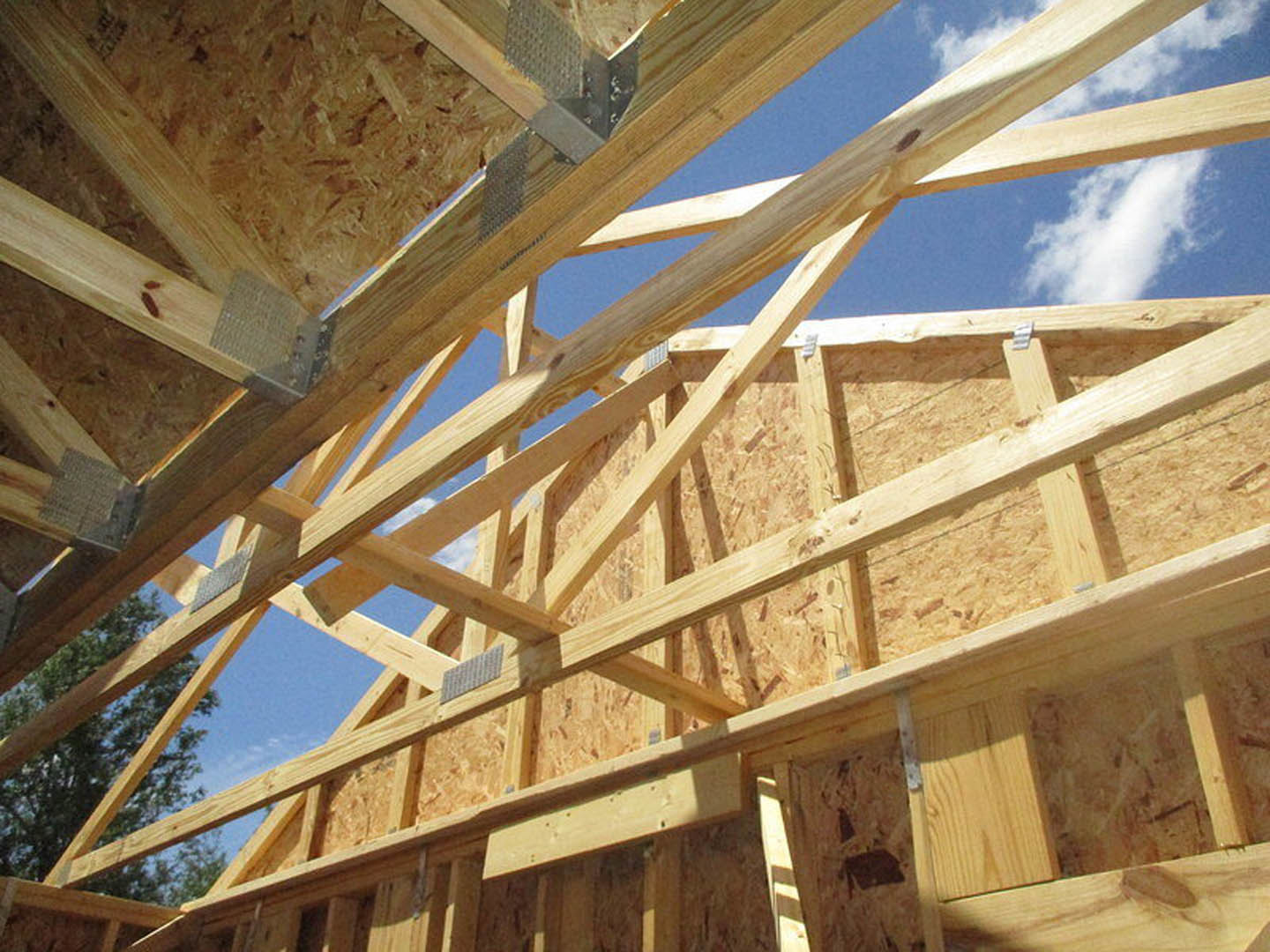 Wooden framing and beams of a house under construction against a blue sky with scattered clouds