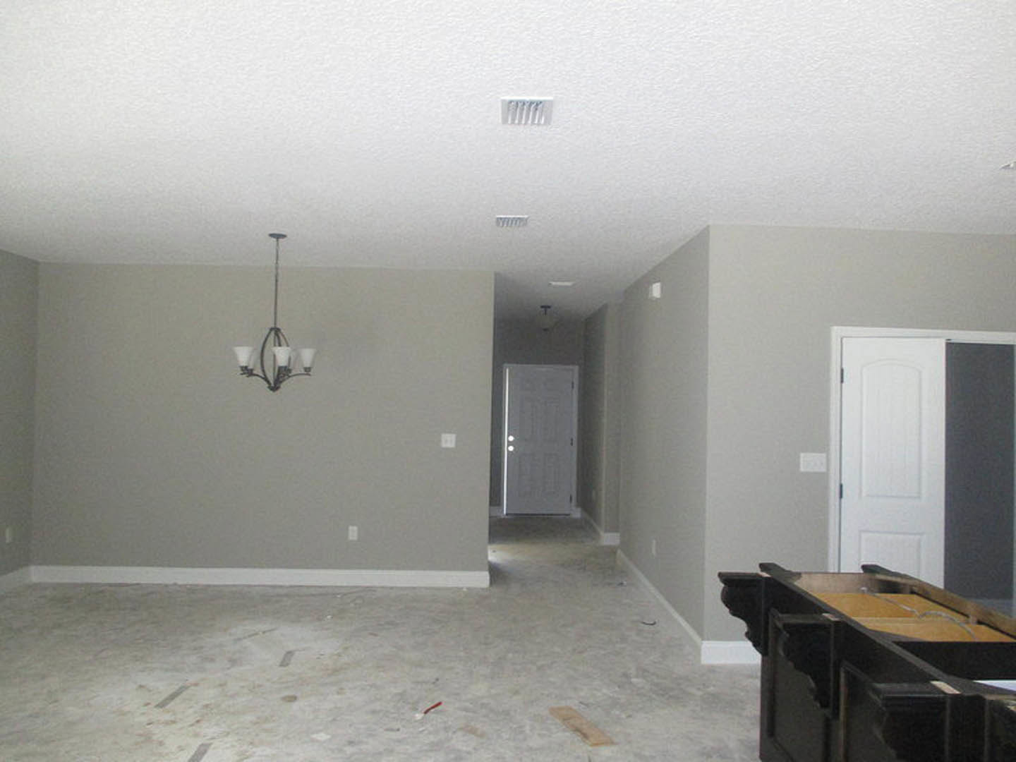 White paneled door in a plaster-walled room, hardwood flooring, ceiling-mounted chandelier, white vent with grey accent, partial view of furniture and table