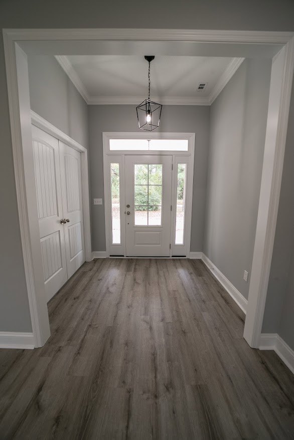 Hallway with wood flooring, white door featuring glass panes and silver knobs, light bulb in a metal cage hanging from ceiling, plaster walls