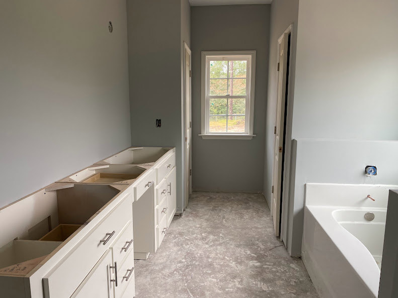 White freestanding bathtub beside a window overlooking trees, gray tile floor, modern sink with chrome faucet, and dark wood cabinetry