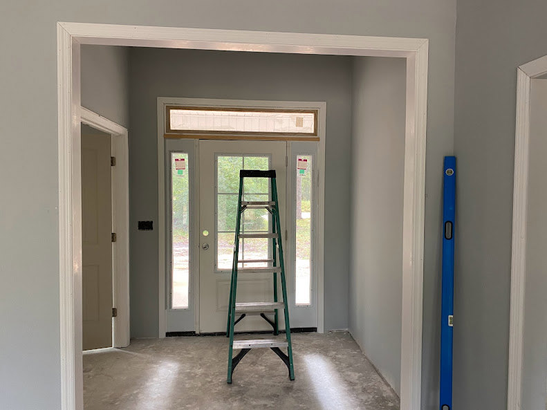 Metal step ladder on smooth concrete floor beside white door, white tiled wall in background, minimalist interior with plaster ceiling and clean finishes