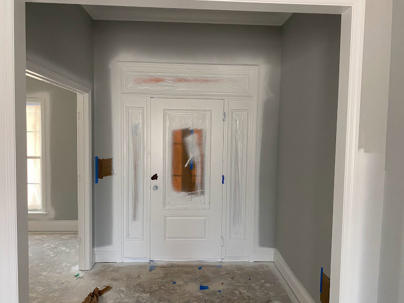 White paneled door with rectangular window, blue painter’s tape applied near handle, white painted walls, light wood flooring, simple molding.