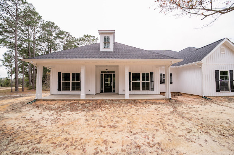 White house with black roof and black door with glass panes, tree branch with green leaves in foreground, multiple windows on exterior, white siding, porch area visible