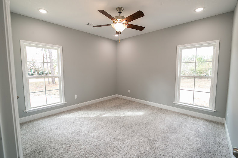 Ceiling fan mounted on white plaster ceiling, large windows with trim, neutral walls, hardwood flooring
