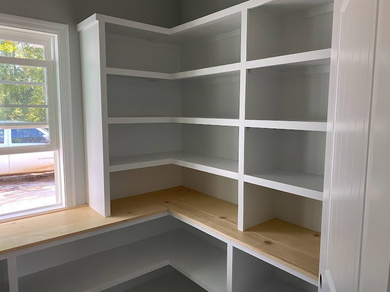 White built-in shelves along a wall in a bright room with large windows and minimal decor