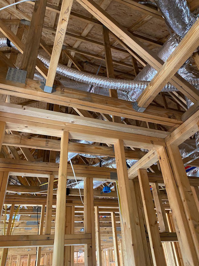 Exposed wood framing and ceiling beams with visible metal ductwork in a house under construction