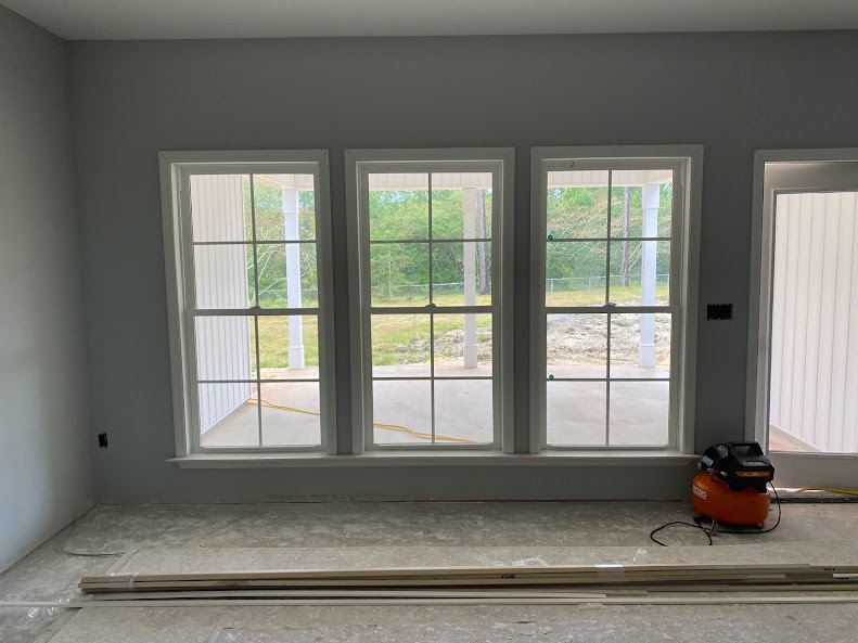 Tile floor room with a row of white-framed windows, vacuum cleaner near the wall, window blinds partially open, view of green yard outside.