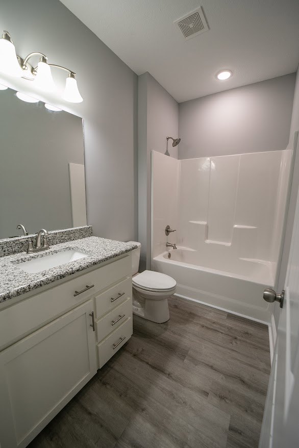 Modern bathroom featuring a white sink with black hardware, white toilet with matching lid, light tile flooring, and neutral wall finishes.