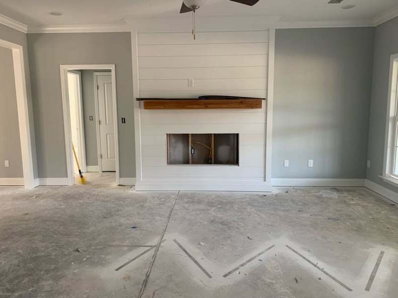Living room with stone fireplace, white plaster walls, wood door, ceiling fan with frosted glass light, and light tile flooring