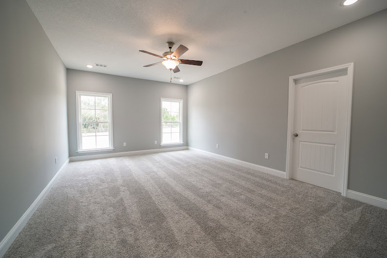 Carpeted room featuring a ceiling fan, white plaster walls, laminate flooring near the doorway, and simple interior finishes.