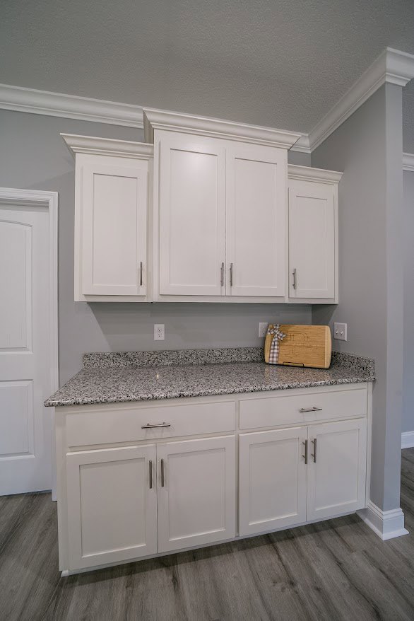White kitchen cabinets with silver handles, marbled granite countertops, stainless steel appliances, white door with matching frame, light-colored flooring.