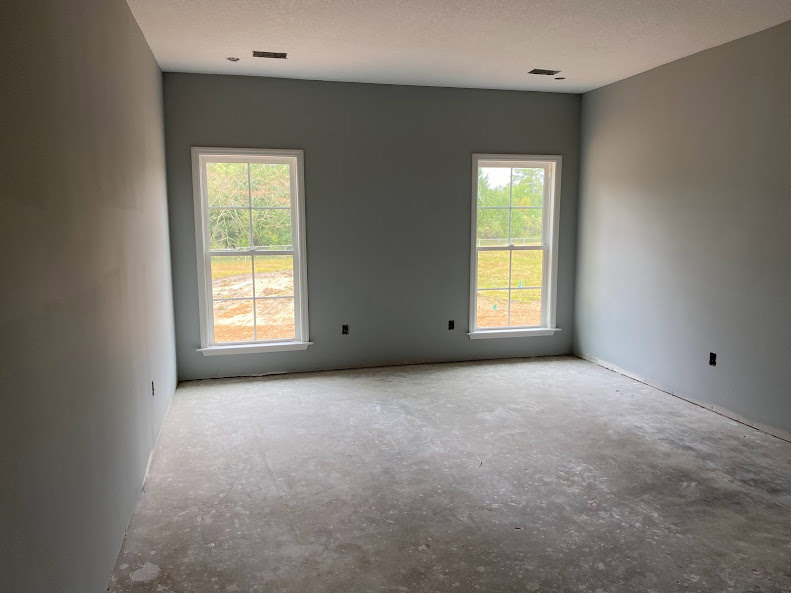 Spacious room with two large windows, concrete flooring, sunlight streaming in, views of grassy field and trees outside