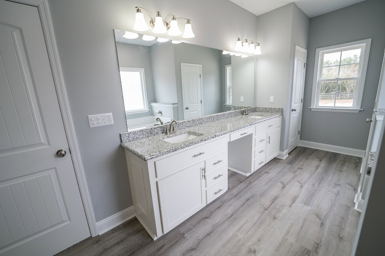Bathroom featuring a double vanity with white sinks, wide frameless mirror, light gray tile flooring, wood cabinetry with drawers, and quartz countertops.