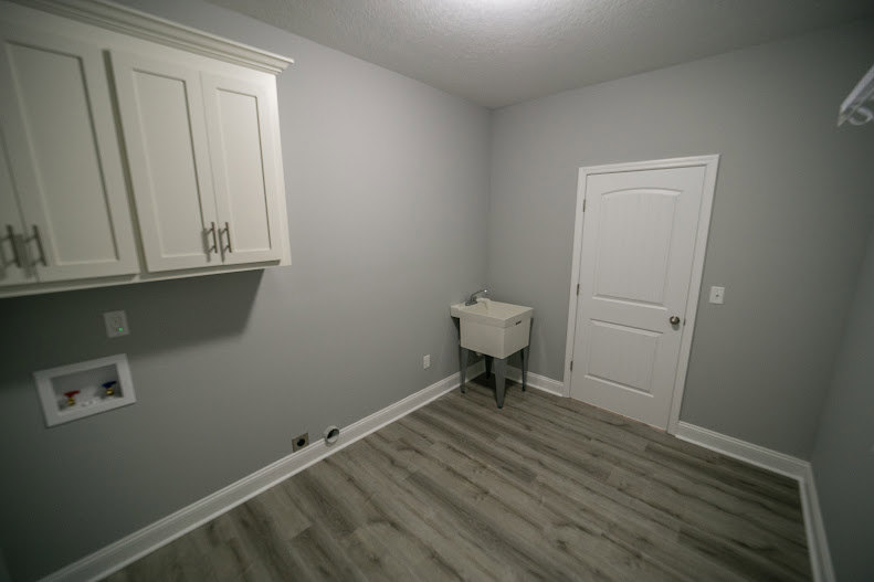 White bathroom sink with chrome faucet set in a vanity, light tile flooring, plaster walls, and a wooden door.