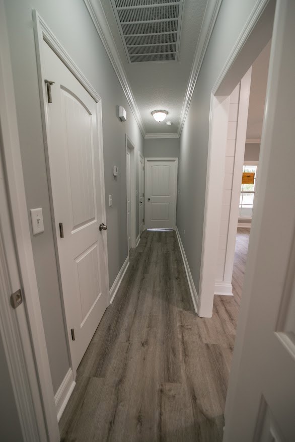 Hallway with white paneled doors, light wood flooring, white plaster walls, and recessed ceiling lighting