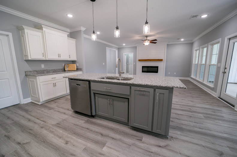 Spacious kitchen featuring a large central island with stone countertop, white cabinetry, stainless steel appliances, tile backsplash, and hardwood flooring