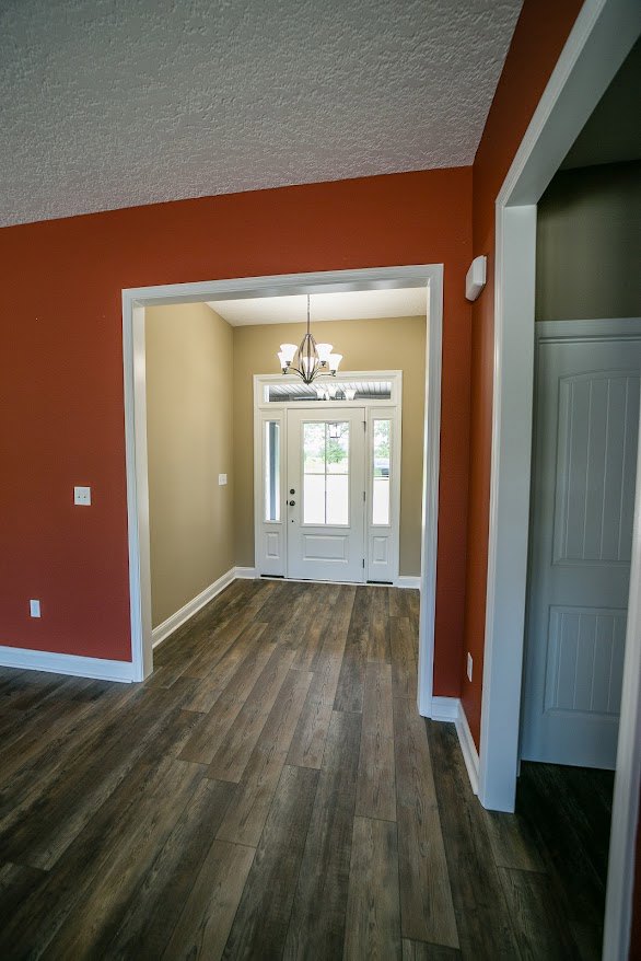 Hallway with wood flooring, white walls, and a white door featuring glass panes; chandelier overhead adds ambient lighting