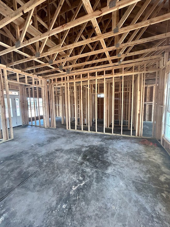 Concrete floor with exposed wood framing, ceiling beams, white door with glass panes, and window with metal bars