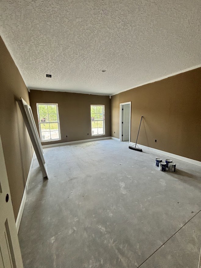 Freshly painted room with tile flooring, paint cans, broom, and ladder; large window framed in white overlooks green grass outside.