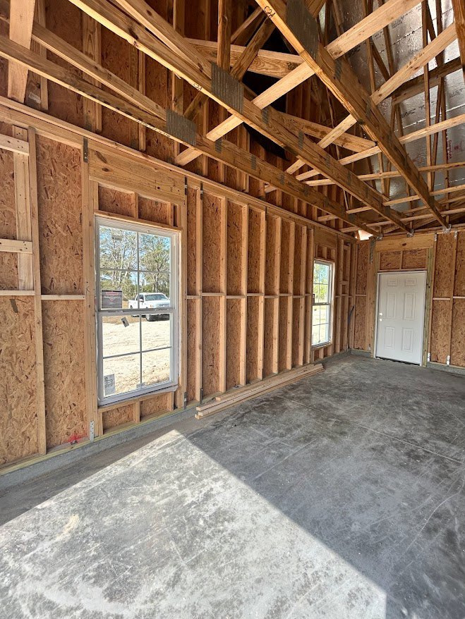 Concrete floor with close-up texture, exposed wooden ceiling beams, white door with multiple knobs, large window overlooking a white truck outside