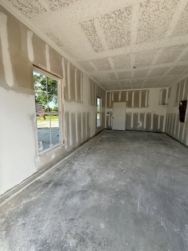 White walls, white door with black handle, concrete floor, window overlooking tree and grass, white paint, black window border