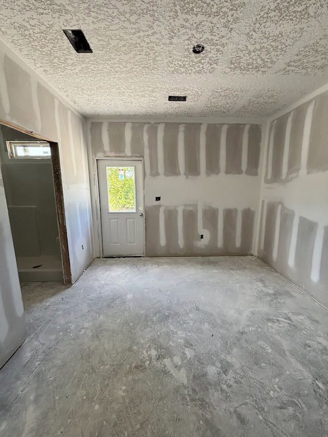 White walls and ceiling, concrete floor, white door with brown frame and window, black ceiling fixture, window with sign