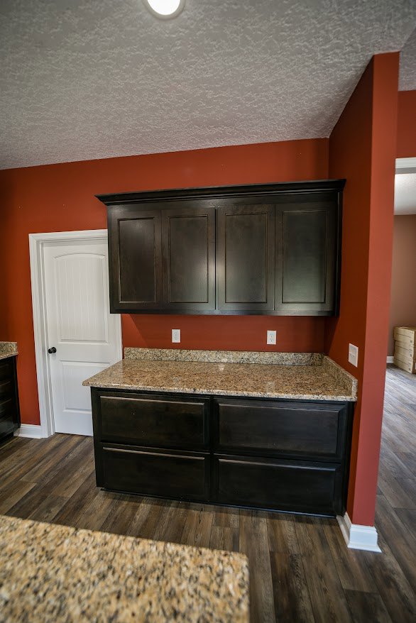 Kitchen with polished granite countertops, wood flooring, white cabinetry with black knobs, stainless steel appliances, and neutral walls